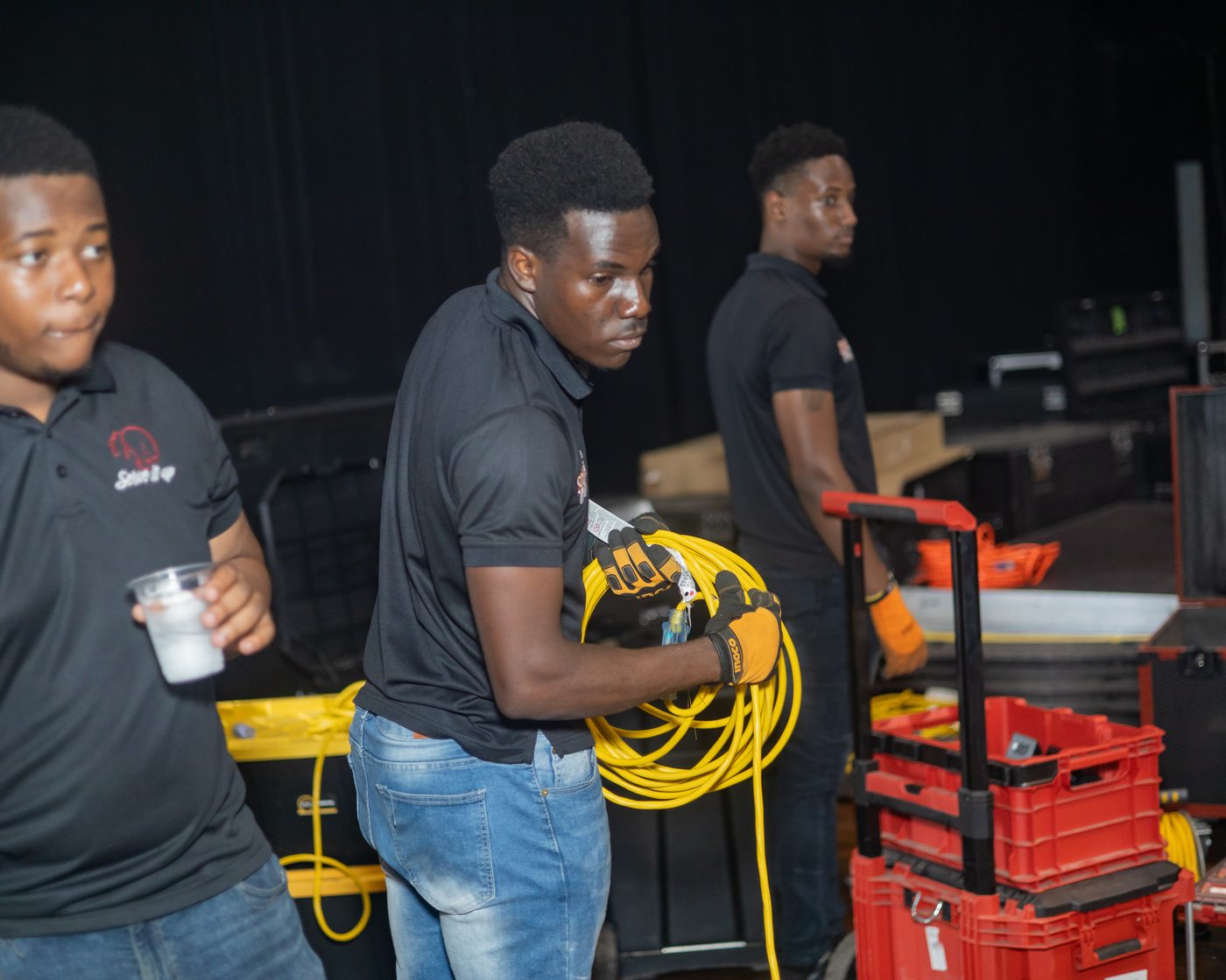 Three of the Sound It Up crew in branded shirts coiling cable during load-in