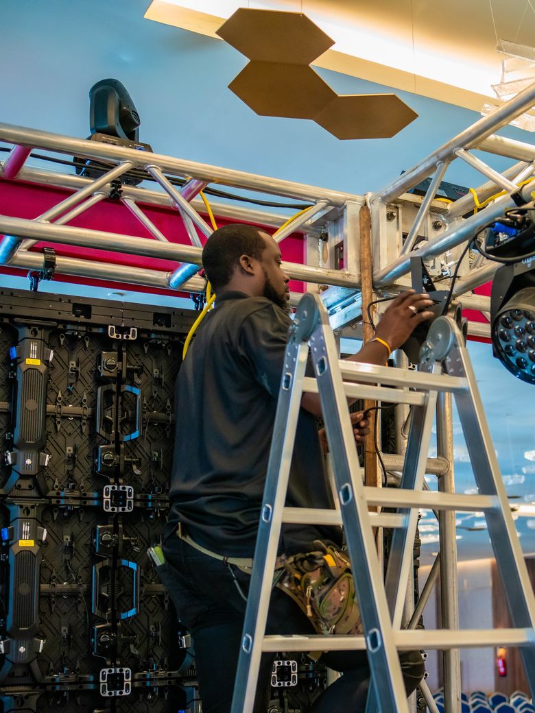 Crew member on a ladder beside the LED wall and moving lights