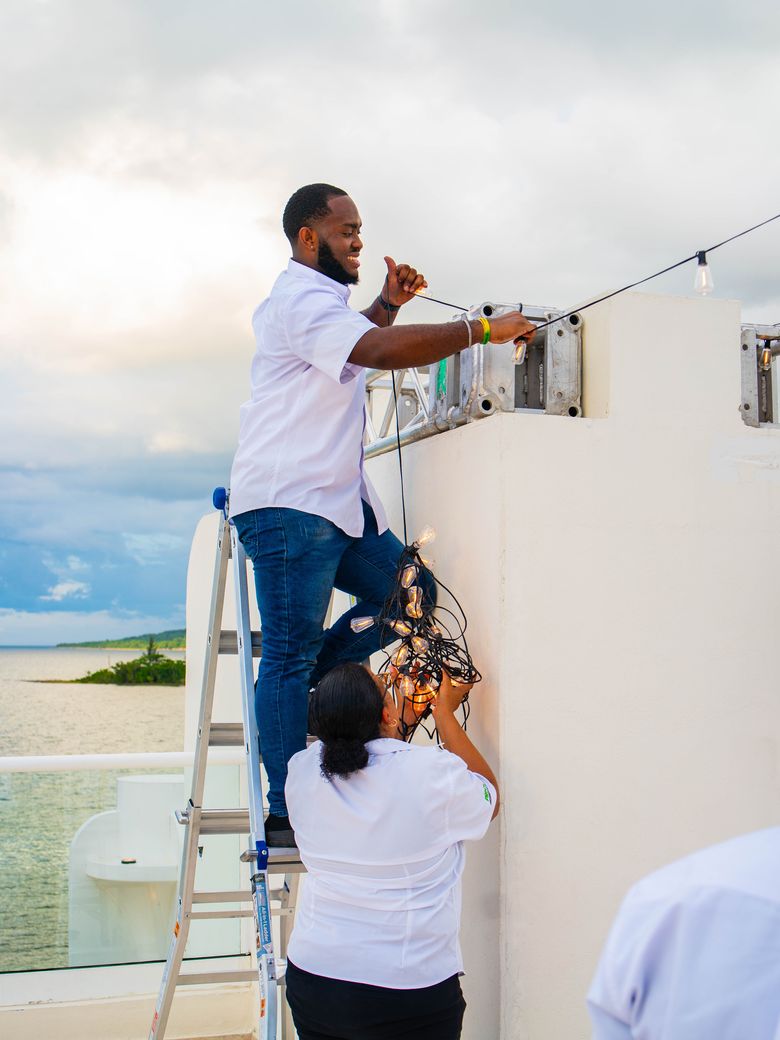 Crew rigging festoon lights on a rooftop terrace by the sea