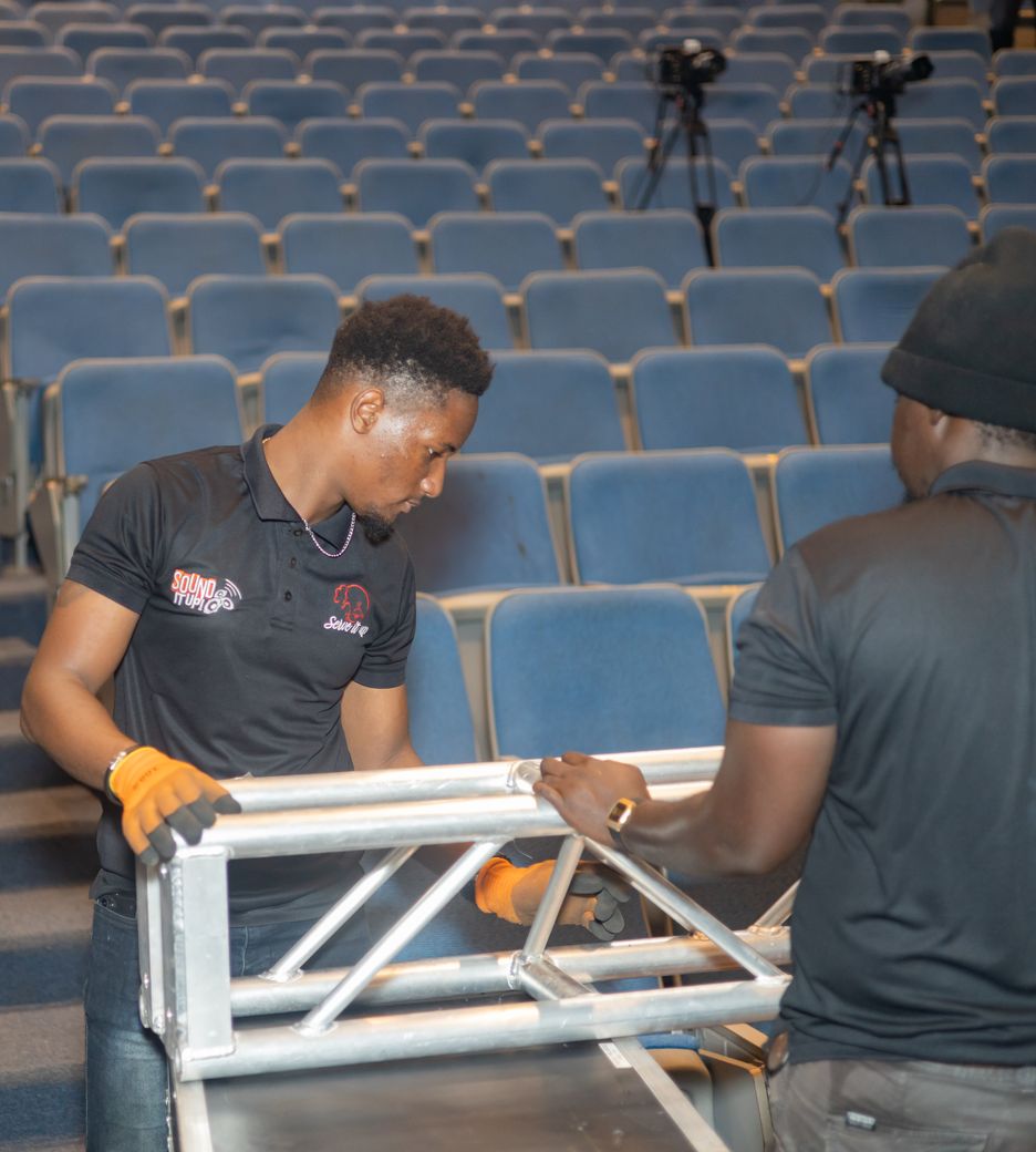 Two Sound It Up crew members carrying a section of truss through the auditorium