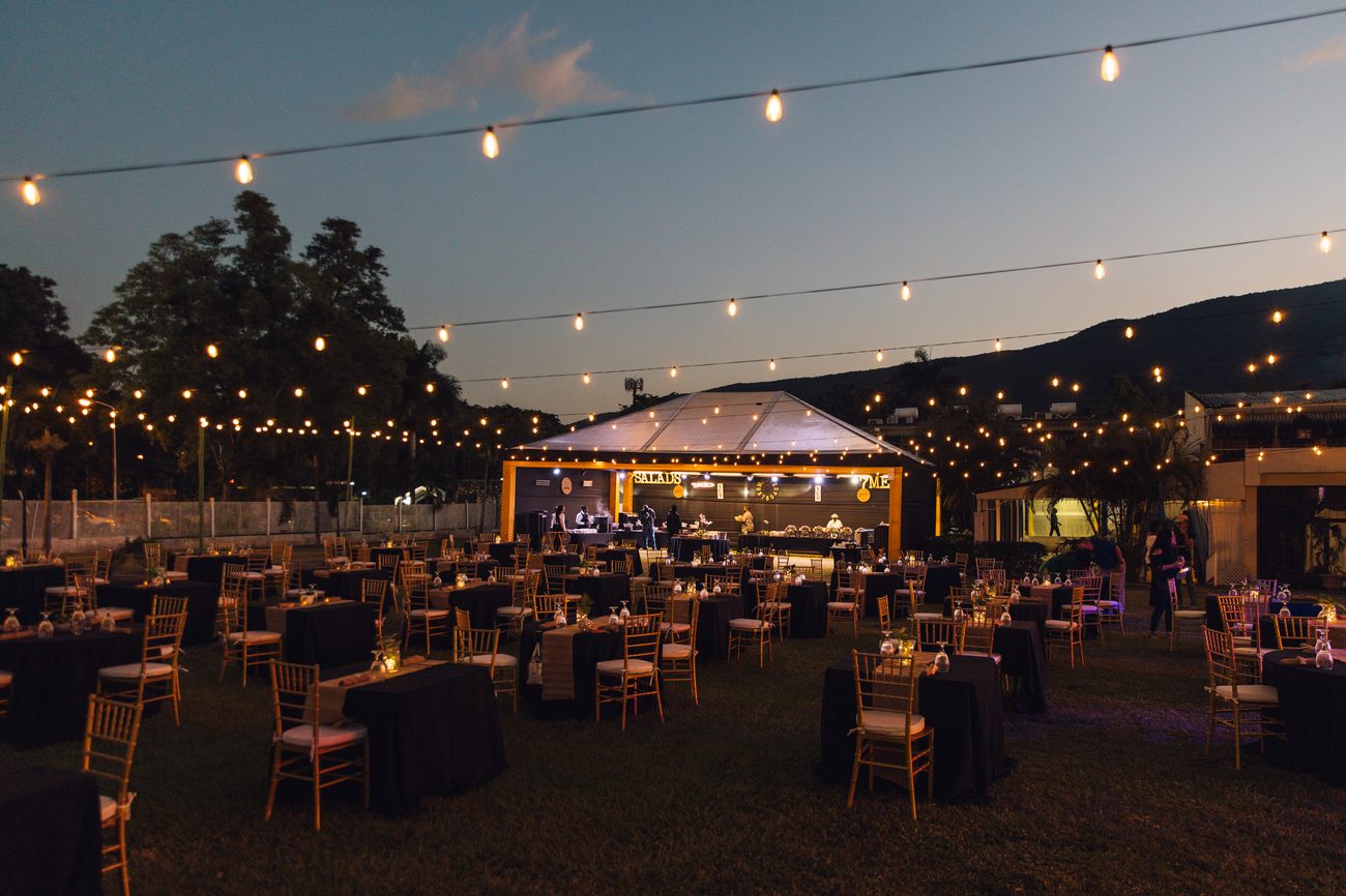 Outdoor venue at dusk lit with festoon lighting over set tables
